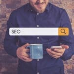 Smiling man holding phone searching for something on Google